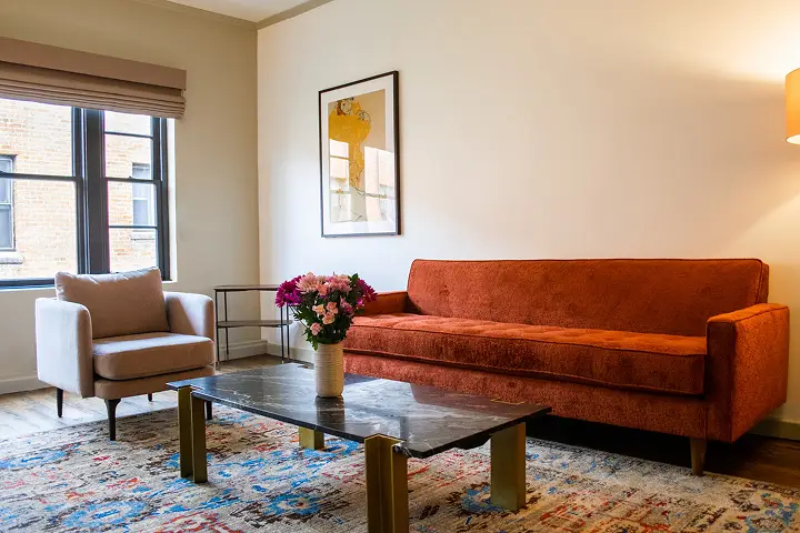 Living room with orange sofa, beige armchair, black coffee table, and warm tones.