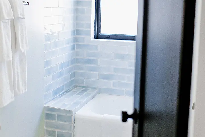 Bathroom with soft blue tiled tub, white towels, and hexagonal floor tiles.