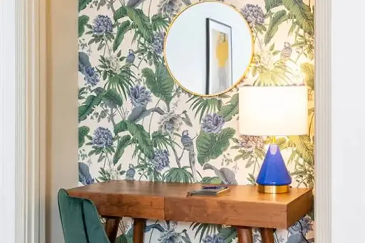 Workspace with wooden desk, green chair, tropical wallpaper, and round mirror.
