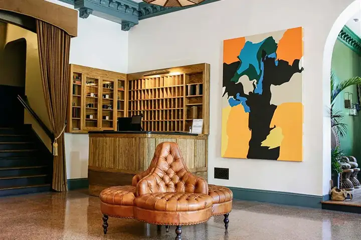 Hotel lobby with leather sofa, bold abstract art, reception desk, and stairs.