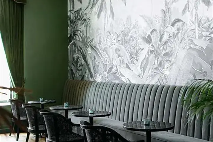 Elegant room with green banquette, tropical wallpaper, and dark round tables.