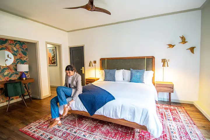 Bedroom with floral wallpaper and person adjusting shoe on the bed.
