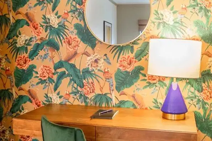Room with floral and bird wallpaper, wooden desk, and green chair.